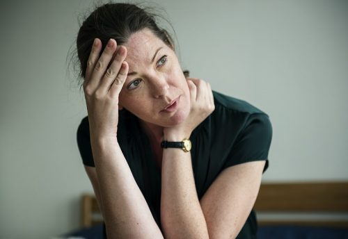 A woman in dark green blouse, holding her head and thinking deeply about her personal issues and problems